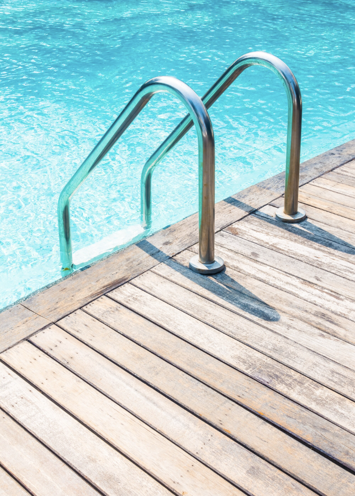 Stainless steel pool ladder with steps at the edge of a clean swimming poo